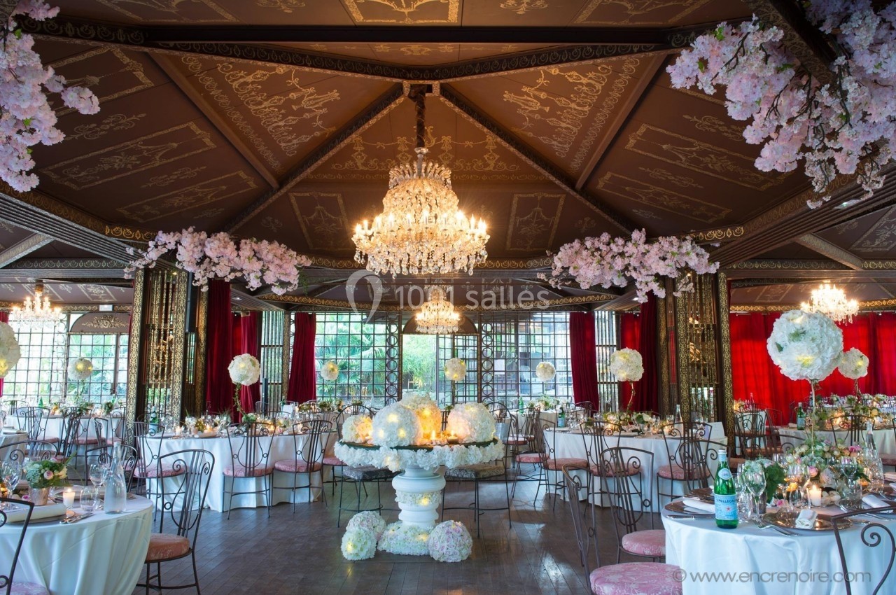 Salle de réception décorée de fleurs blanches, lustres en cristal suspendus et tables rondes élégamment dressées.