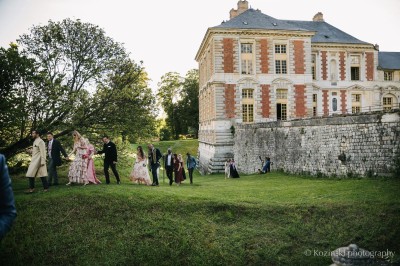 Un groupe de femmes en robes élégantes réagit avec joie face à une mariée dans une pièce décorée.