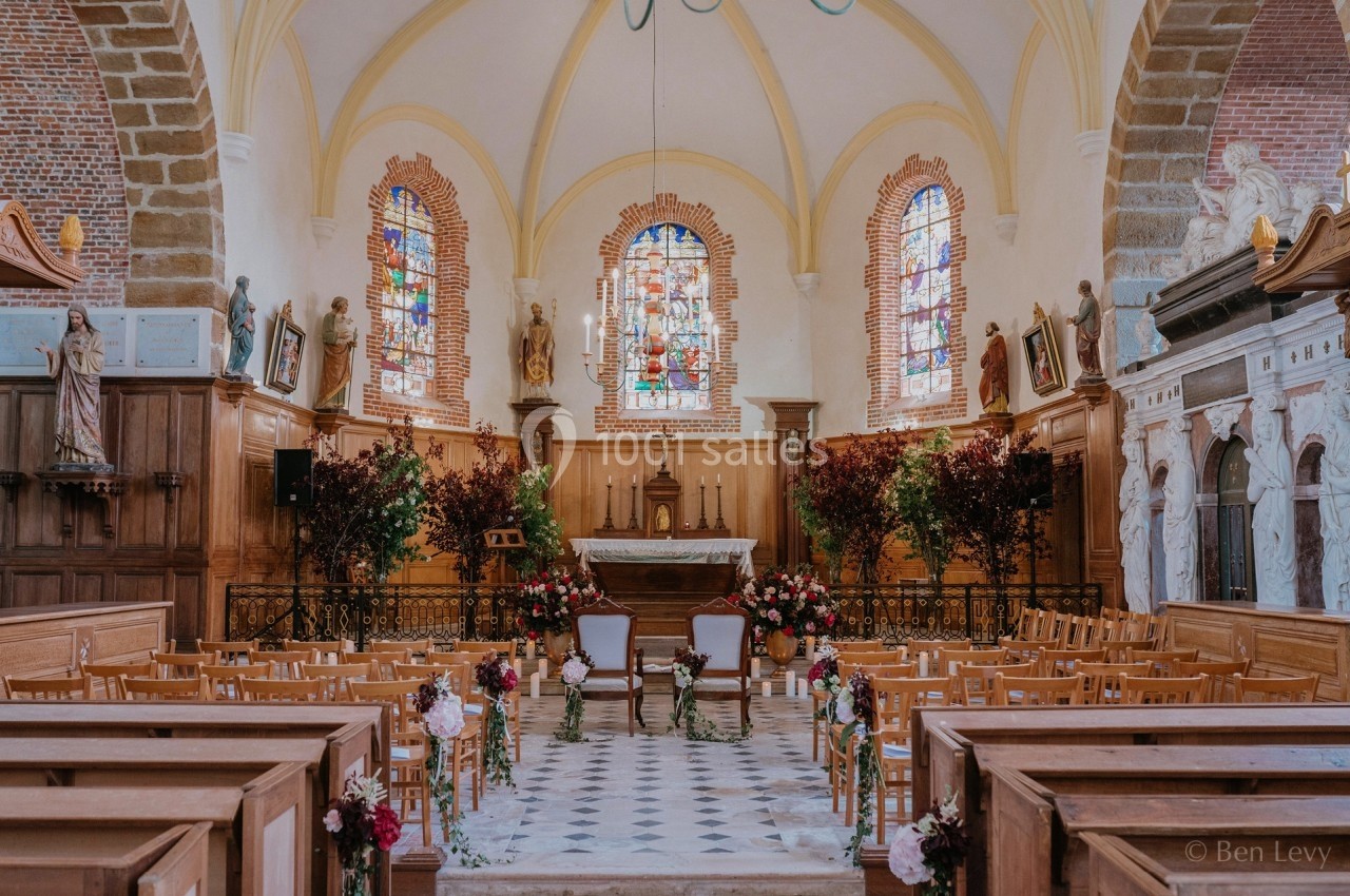 Intérieur d'une église avec des bancs en bois, un autel décoré de fleurs et des vitraux colorés.