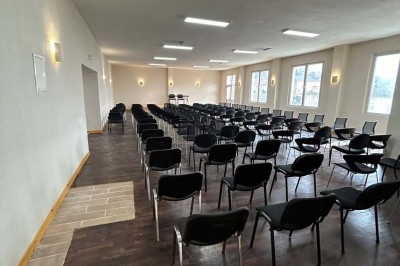 Des personnes, dont des enfants, entrent dans un bâtiment à façade claire avec des fenêtres et une porte ouverte.