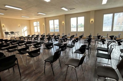 Des personnes, dont des enfants, entrent dans un bâtiment à façade claire avec des fenêtres et une porte ouverte.