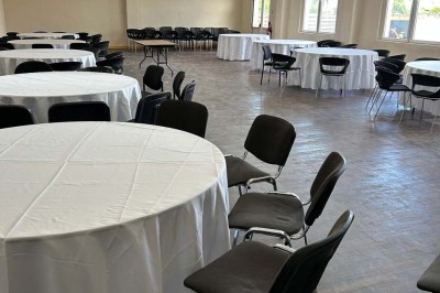 Des personnes, dont des enfants, entrent dans un bâtiment à façade claire avec des fenêtres et une porte ouverte.