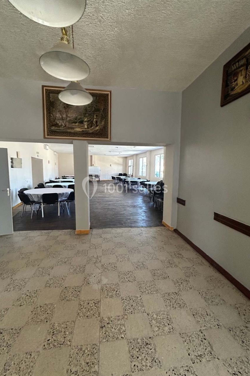 Salle avec sol carrelé, tables et chaises disposées dans une pièce lumineuse visible à travers une ouverture.