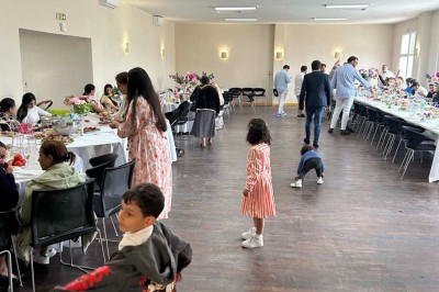 Des personnes, dont des enfants, entrent dans un bâtiment à façade claire avec des fenêtres et une porte ouverte.