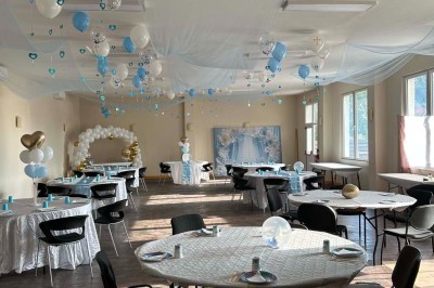 Des personnes, dont des enfants, entrent dans un bâtiment à façade claire avec des fenêtres et une porte ouverte.