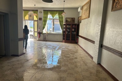 Des personnes, dont des enfants, entrent dans un bâtiment à façade claire avec des fenêtres et une porte ouverte.