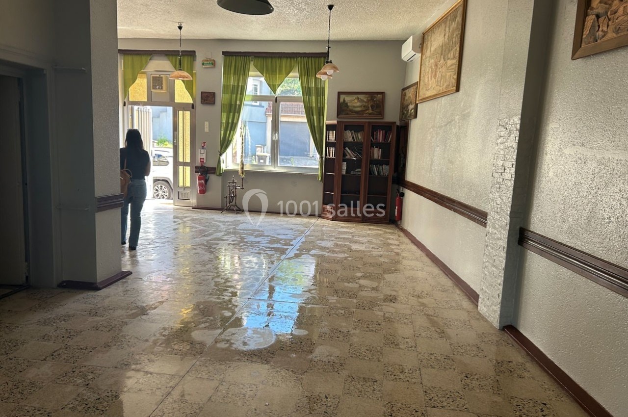 Intérieur d'une pièce lumineuse avec sol en carrelage, étagère, tableaux muraux et une personne près de la sortie.