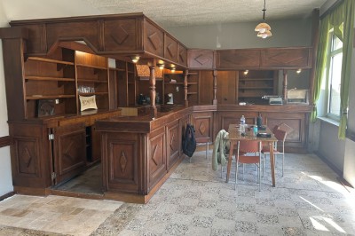 Des personnes, dont des enfants, entrent dans un bâtiment à façade claire avec des fenêtres et une porte ouverte.