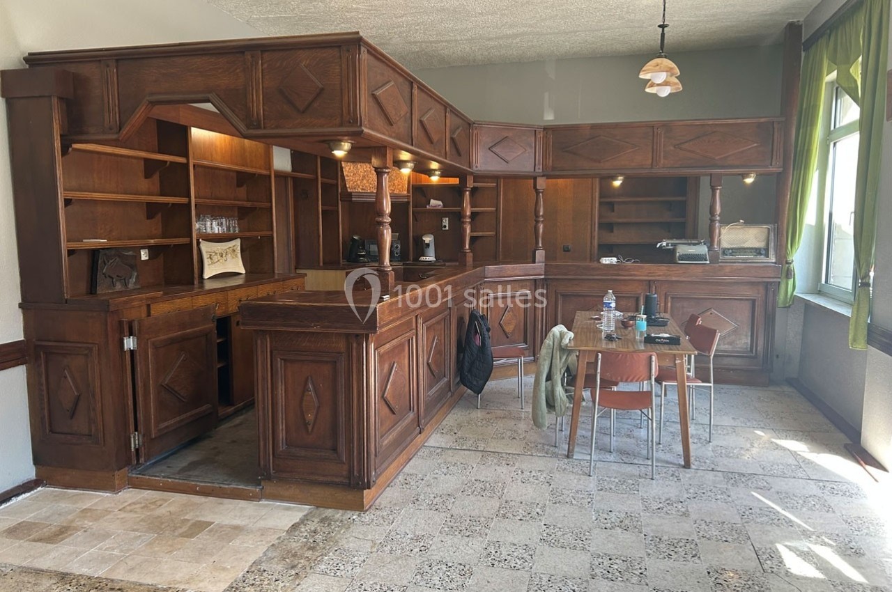 Cuisine en bois sombre avec un bar intégré, table et chaises au centre, lumière naturelle entrant par une fenêtre.