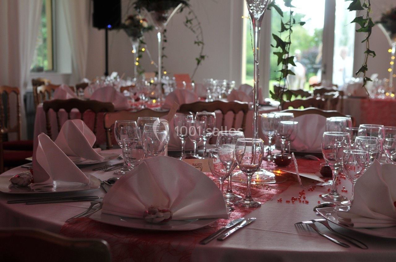 Table élégamment dressée avec nappes blanches, serviettes pliées, verres et couverts dans une salle lumineuse.
