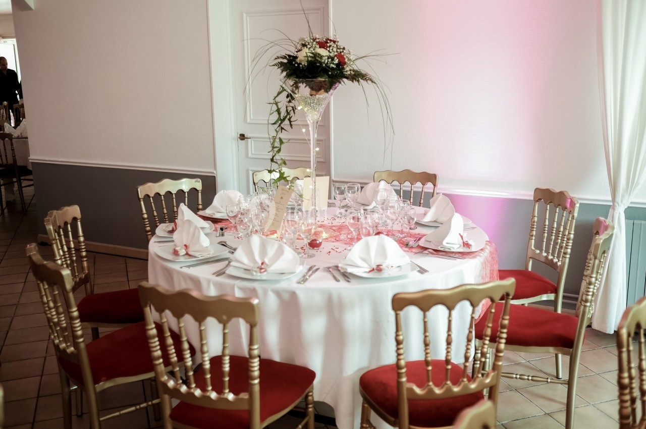 Table ronde décorée pour un événement, avec nappes blanches, serviettes pliées, vaisselle et centre de table floral.