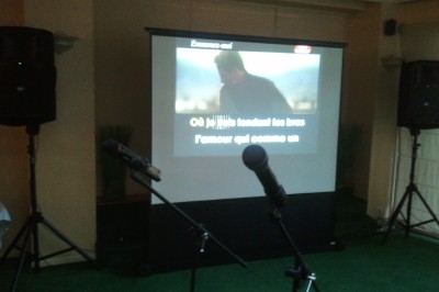 Une mariée en robe blanche descend d'un hélicoptère, aidée par un homme en costume clair, sur une pelouse verte.