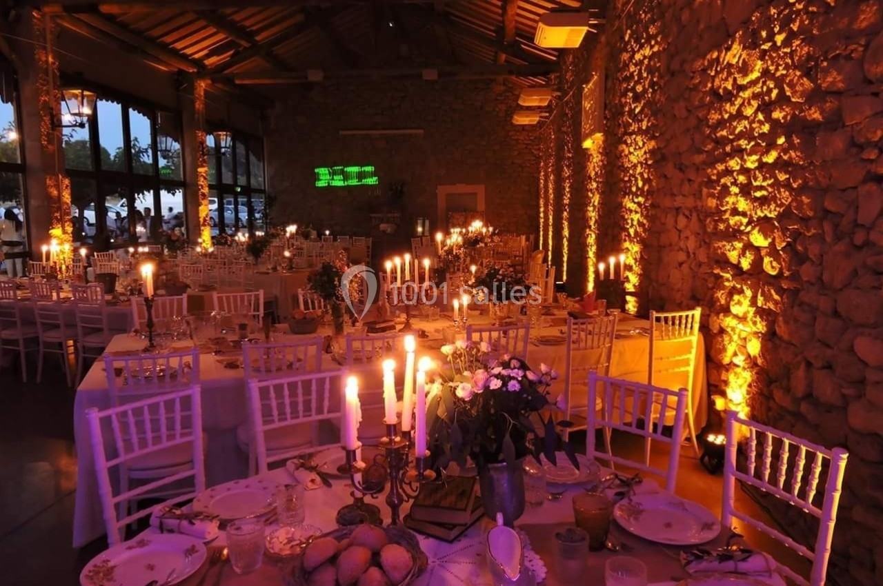 Salle de réception en soirée avec tables décorées, chandeliers allumés et murs en pierre éclairés par des lumières chaudes.