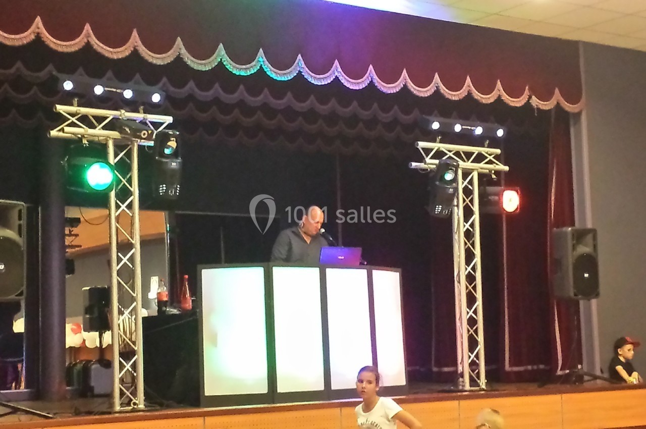 Un DJ mixe sur une scène éclairée avec des projecteurs colorés, entouré d'équipements sonores et lumineux.