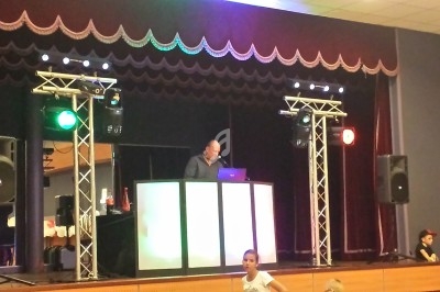 Un DJ mixe sur une scène éclairée, entouré de projecteurs et de structures lumineuses, dans une salle de spectacle.