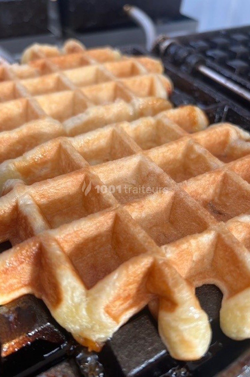 Gaufre dorée en cours de cuisson sur un gaufrier noir, avec une texture croustillante et alvéolée visible.