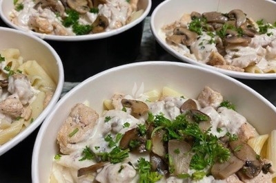 Burger au saumon fumé avec laitue, tomate et sauce, posé sur une table en marbre avec citron vert et herbes en arrière-plan.