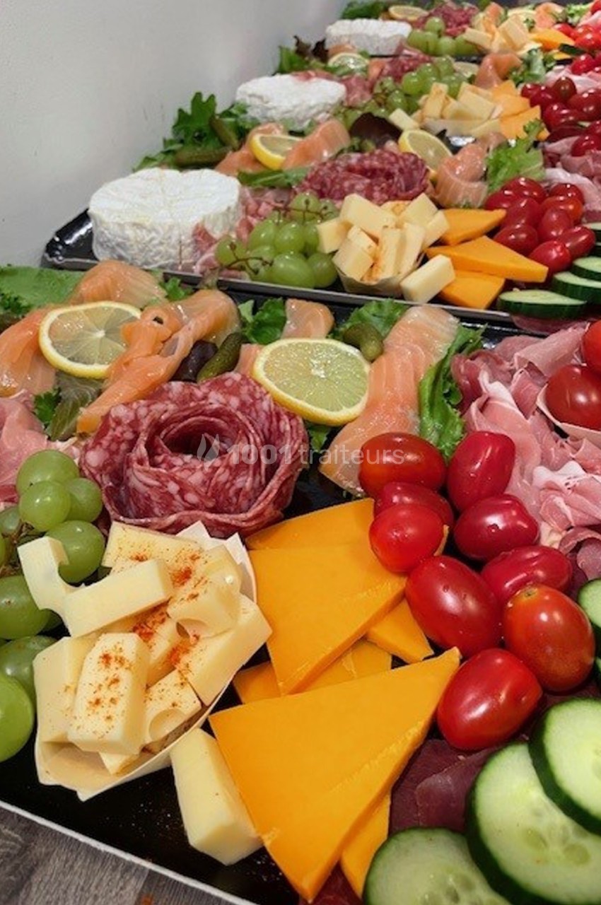 Plateau varié de charcuteries, fromages, fruits et légumes frais disposés sur un fond noir.