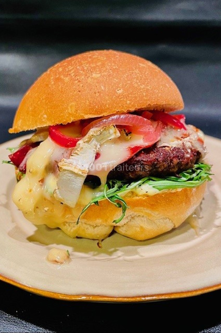 Burger garni de fromage fondu, oignons rouges, salade et viande, présenté sur une assiette beige.