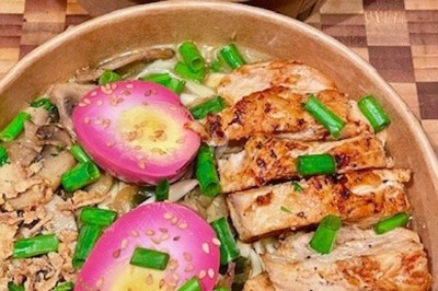 Burger au saumon fumé avec laitue, tomate et sauce, posé sur une table en marbre avec citron vert et herbes en arrière-plan.