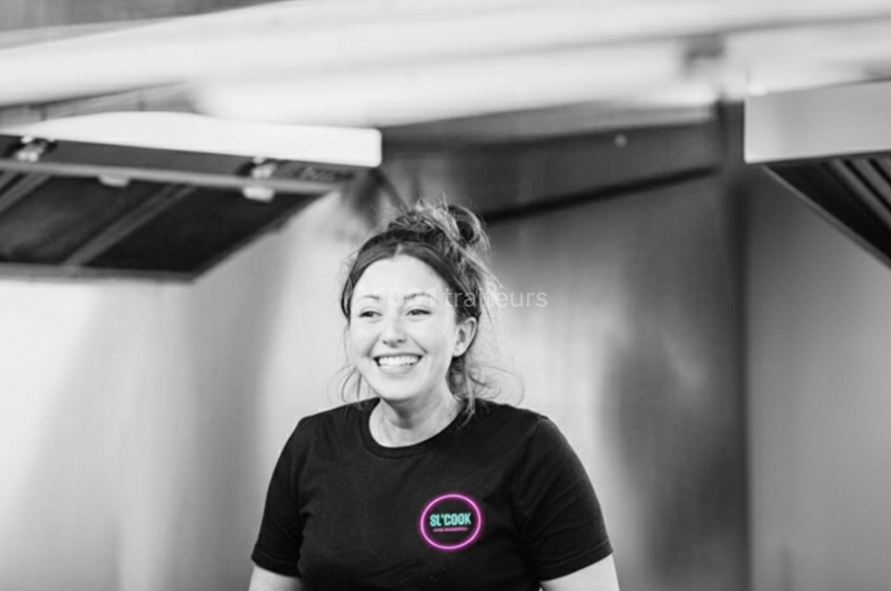 Femme souriante portant des gants noirs, travaillant dans une cuisine professionnelle.