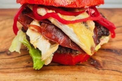 Burger au saumon fumé avec laitue, tomate et sauce, posé sur une table en marbre avec citron vert et herbes en arrière-plan.