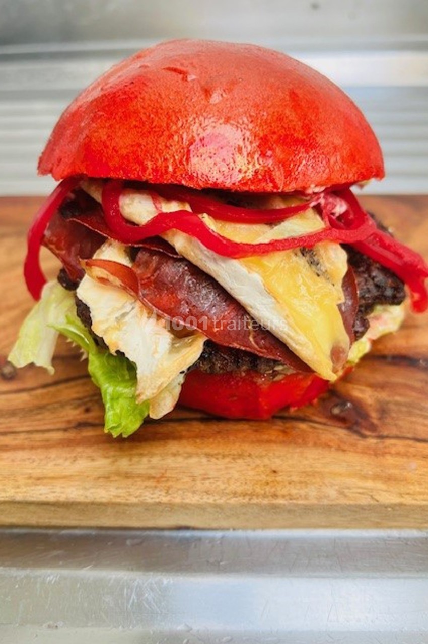 Burger avec pain rouge, garni de viande, fromage fondu, salade, poulet et rondelles de poivron rouge.