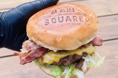 Burger au saumon fumé avec laitue, tomate et sauce, posé sur une table en marbre avec citron vert et herbes en arrière-plan.