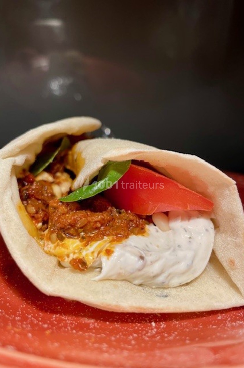 Sandwich pita garni de sauce blanche, tomate, basilic et préparation à base de tomate, présenté sur une assiette rouge.