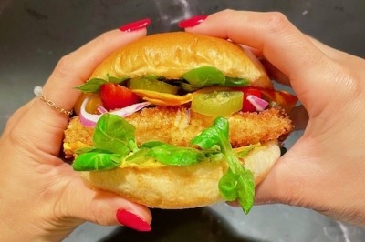 Burger au saumon fumé avec laitue, tomate et sauce, posé sur une table en marbre avec citron vert et herbes en arrière-plan.