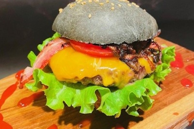 Burger au saumon fumé avec laitue, tomate et sauce, posé sur une table en marbre avec citron vert et herbes en arrière-plan.