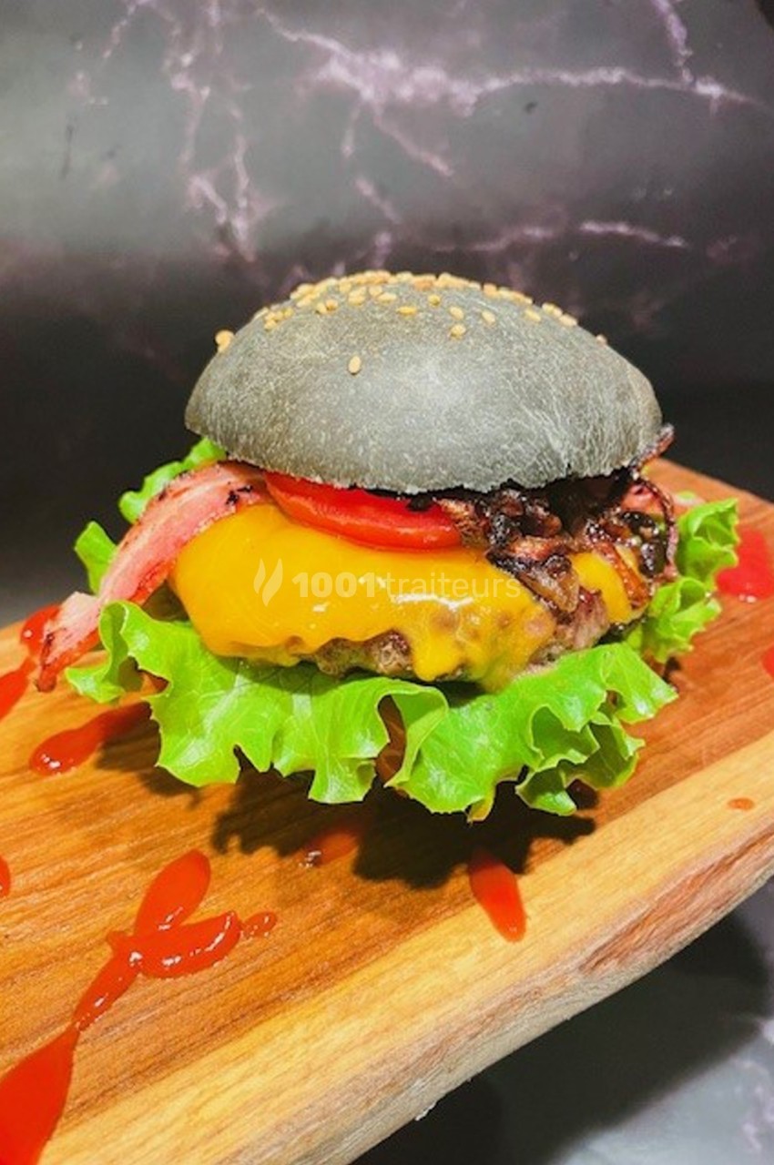 Burger avec pain noir, steak, fromage fondu, tomate, laitue et bacon, présenté sur une planche en bois.