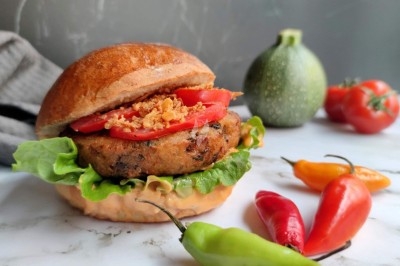 Burger au saumon fumé avec laitue, tomate et sauce, posé sur une table en marbre avec citron vert et herbes en arrière-plan.