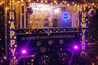 Food truck décoré avec des guirlandes lumineuses et des inscriptions ’Happy New Year’, stationné sur des pavés la nuit.