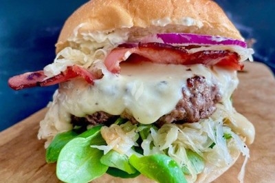 Burger garni de fromage fondu, bacon, oignons rouges, salade et choucroute, posé sur une planche en bois.