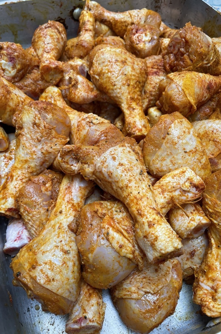 Pilons de poulet marinés avec des épices, disposés dans un grand plat métallique.