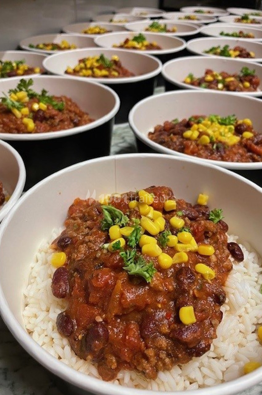 Assiettes de riz garnies de chili con carne, haricots rouges, maïs et persil, alignées sur une table.