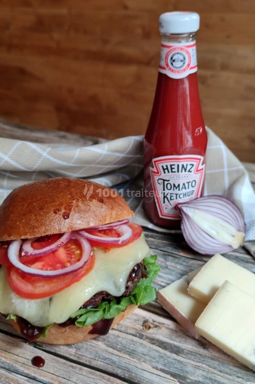 Burger garni de fromage fondu, laitue, rondelles de tomate et d'oignon, avec une bouteille de ketchup en arrière-plan.
