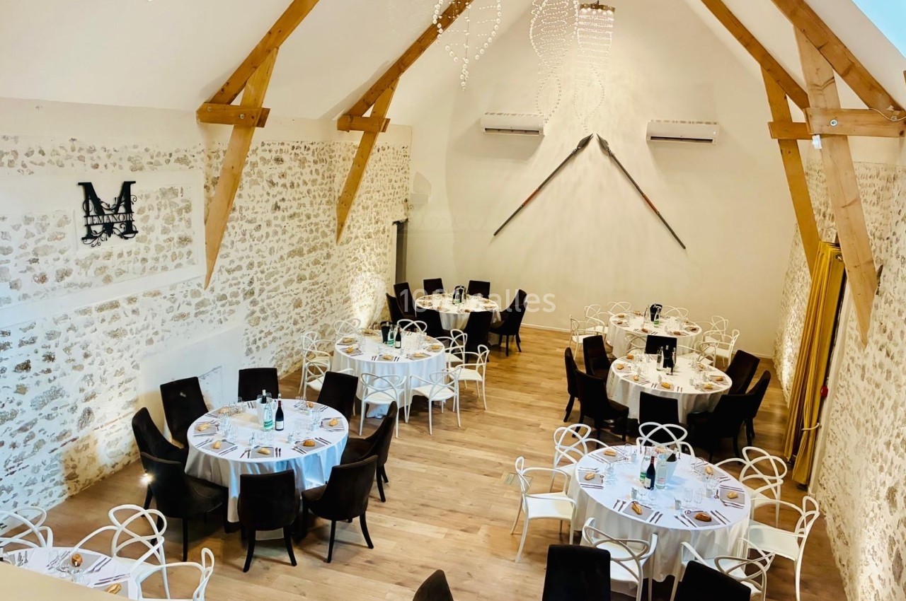 Salle de réception lumineuse avec murs en pierre, poutres apparentes et tables rondes dressées pour un repas.