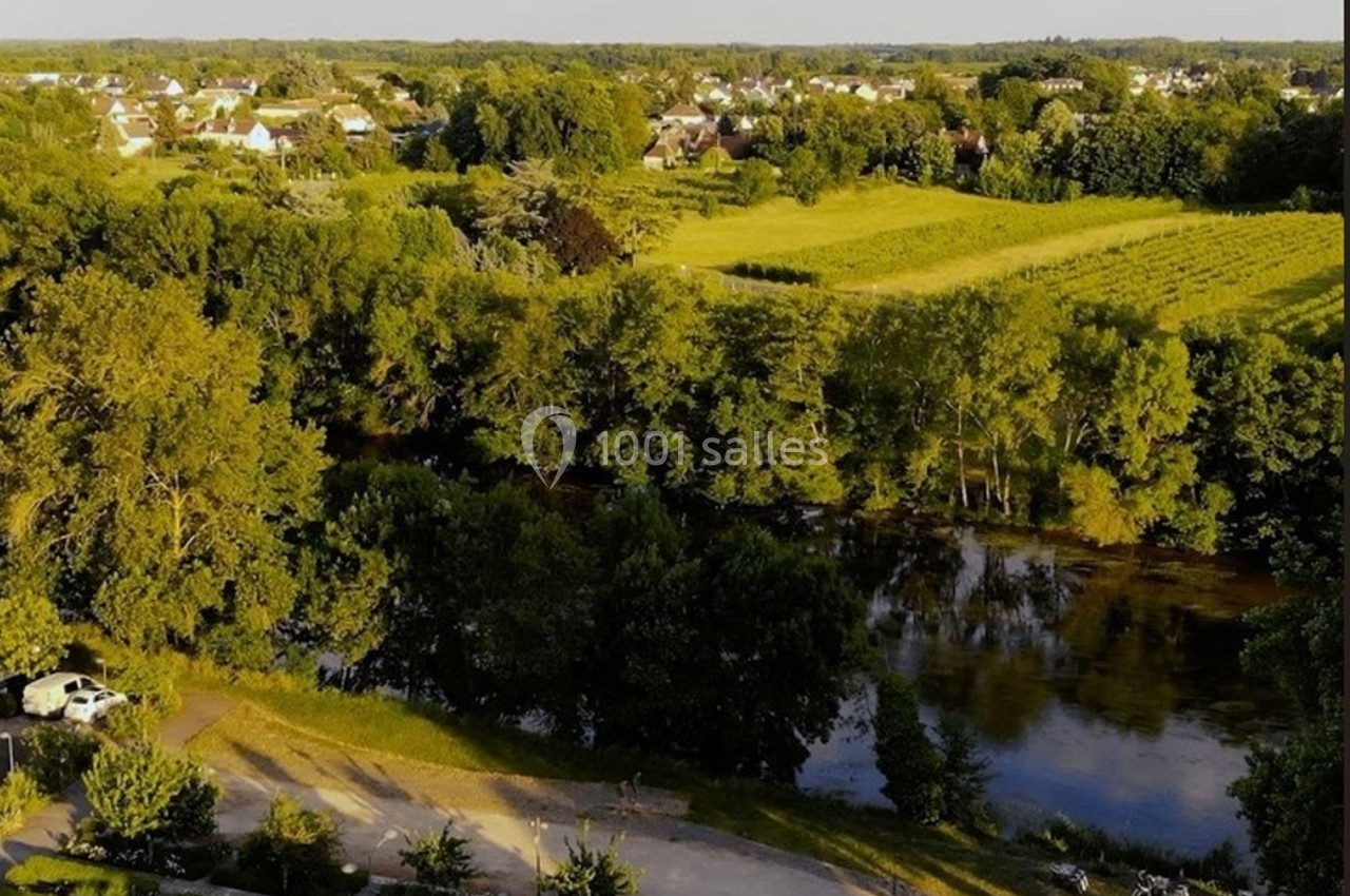 Vue aérienne d'une campagne verdoyante avec des champs, des arbres, une rivière et des habitations au loin.