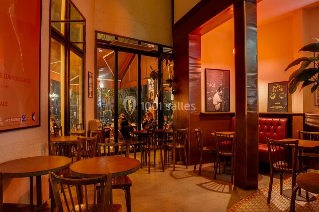 Salle de café chaleureuse avec tables en bois, éclairage tamisé et affiches sur les murs.