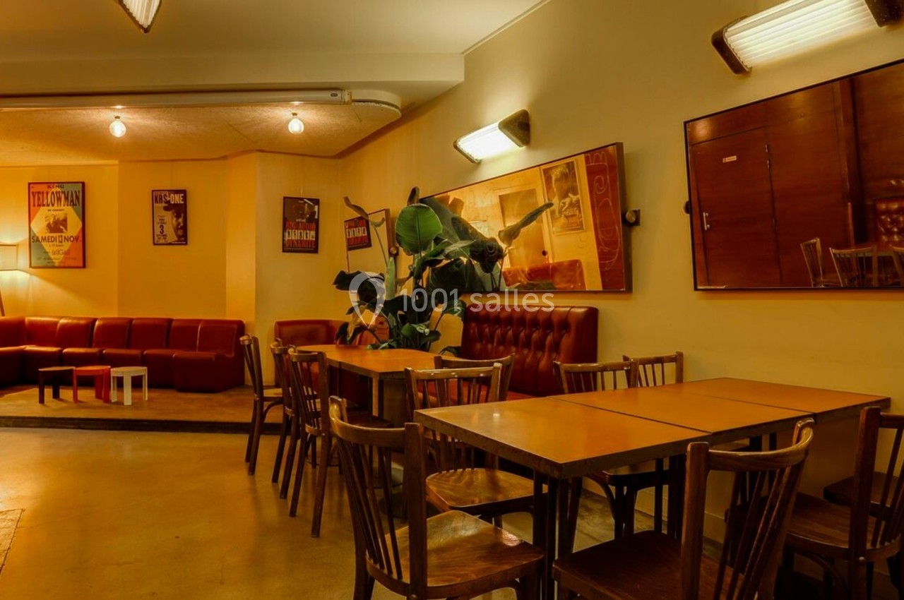 Salle chaleureuse avec tables en bois, chaises assorties, banquettes rouges et affiches encadrées sur les murs.