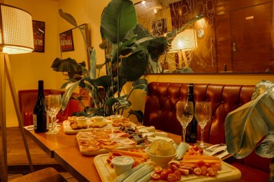 Table dressée dans un restaurant chaleureux avec planches de charcuterie, fromages, légumes et bouteilles de vin rouge.