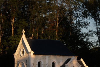 Chambre avec lit double, poutres apparentes, linge de lit blanc, et salle de bain attenante visible par une porte ouverte.