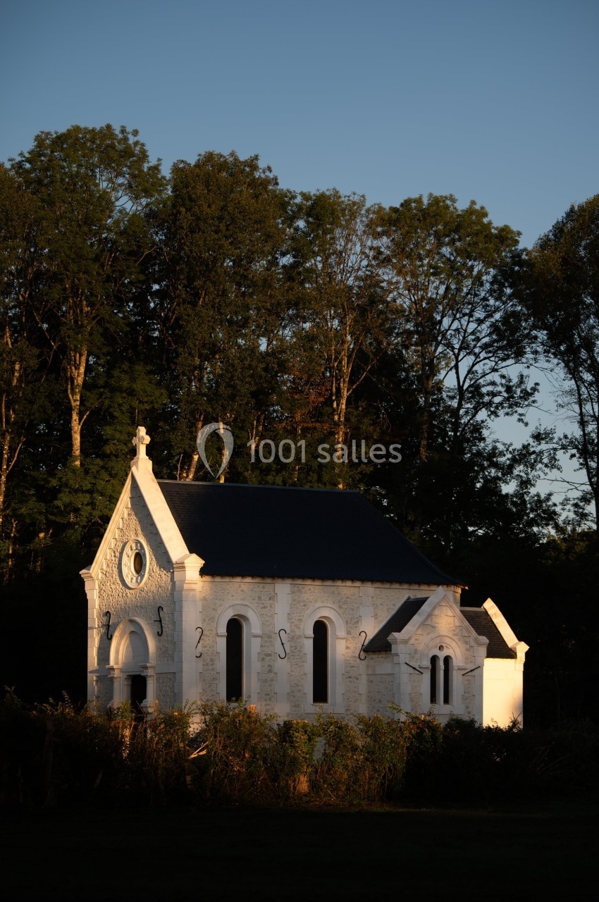 Petite chapelle blanche entourée de végétation, éclairée par une lumière douce au coucher du soleil, avec des arbres en…