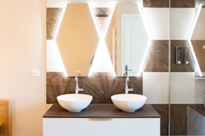 Chambre avec lit double, poutres apparentes, linge de lit blanc, et salle de bain attenante visible par une porte ouverte.