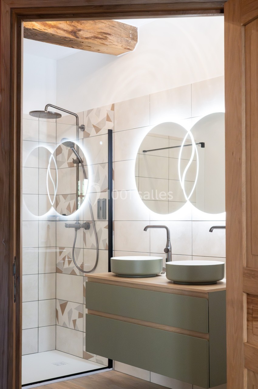 Salle de bain moderne avec douche à l'italienne, vasques doubles et miroirs éclairés, décorée de tons naturels.