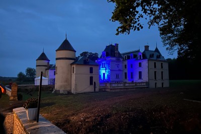 Chambre avec lit double, poutres apparentes, linge de lit blanc, et salle de bain attenante visible par une porte ouverte.