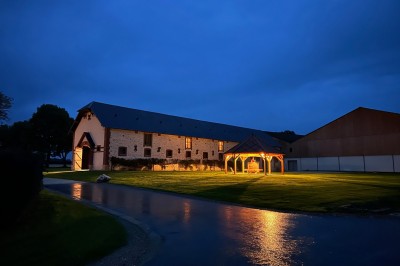Chambre avec lit double, poutres apparentes, linge de lit blanc, et salle de bain attenante visible par une porte ouverte.