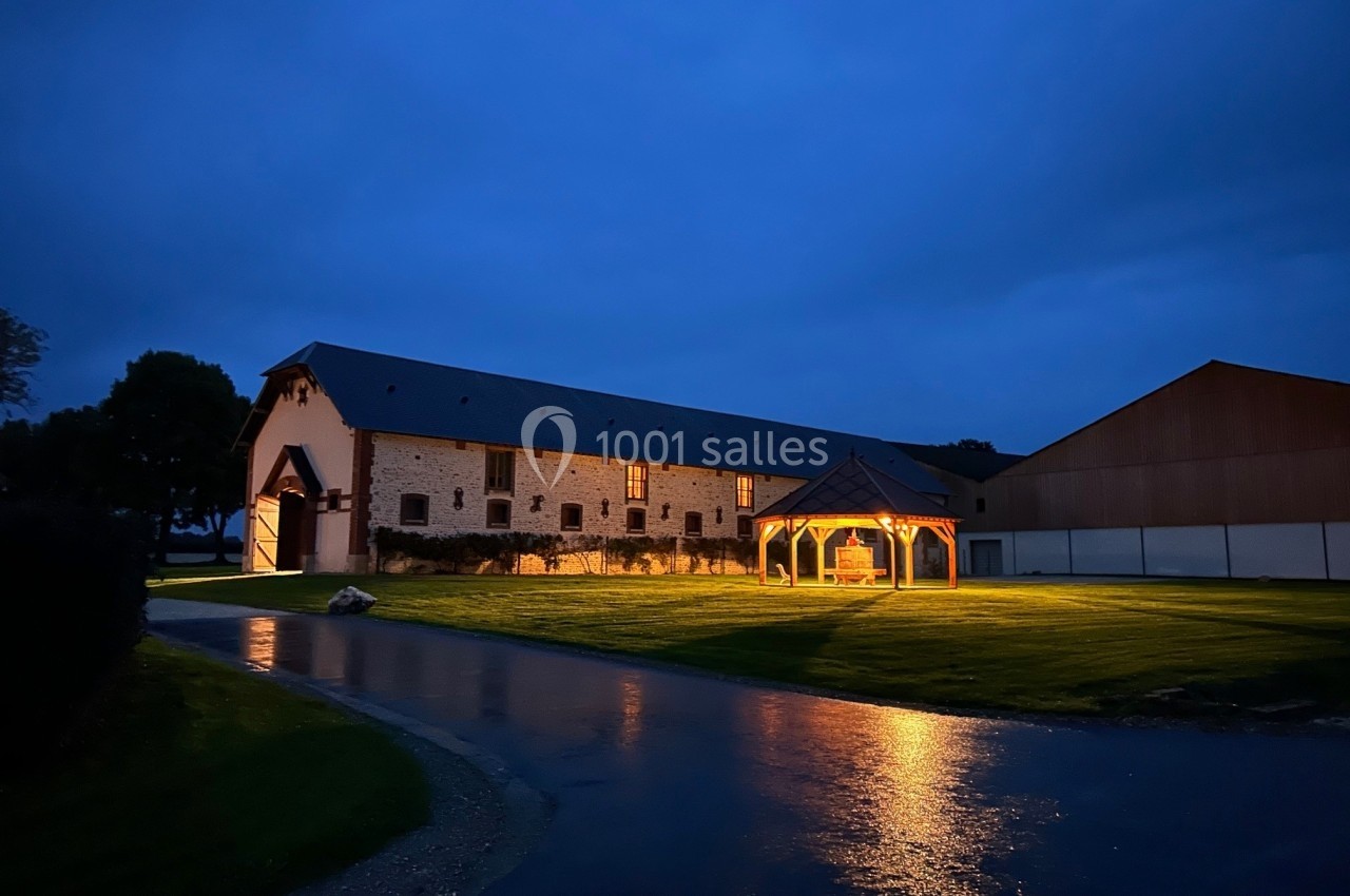 Bâtiment en pierre éclairé de nuit avec une structure en bois illuminée sur une pelouse humide.